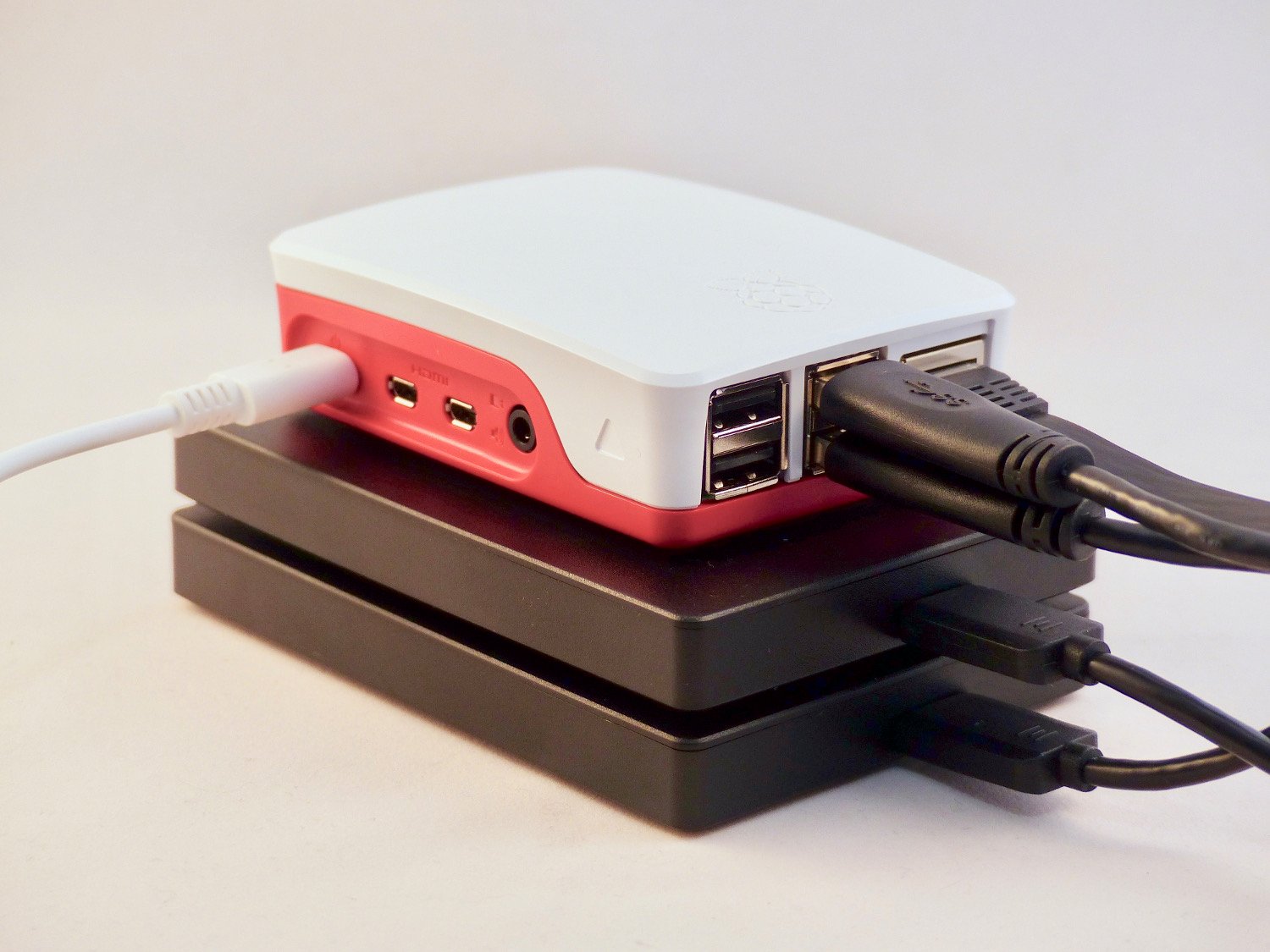 A Raspberry Pi case stacked on top of two external 2.5” hard drives. Multiple USB and Ethernet cables are plugged into the Pi, suggesting it is configured as a compact network-attached storage (NAS) system capable of storing large amounts of data.